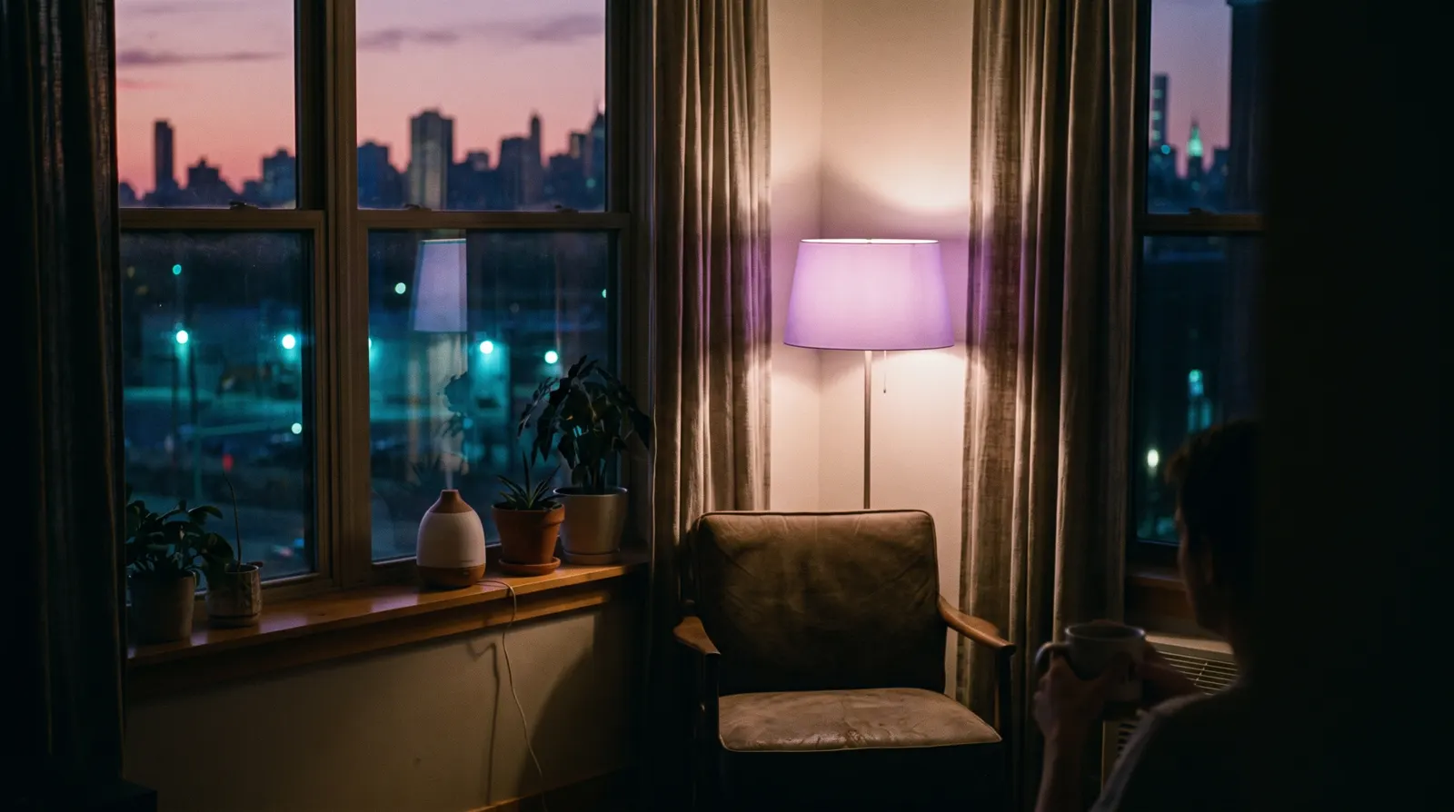 A dim city apartment window at dusk with fading rose and aubergine light.