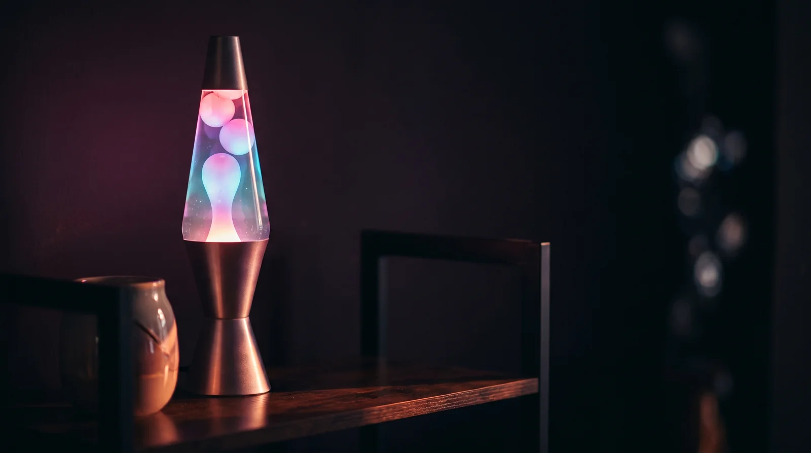 A glowing lava lamp with rose and lavender wax blobs rising against a deep aubergine background.