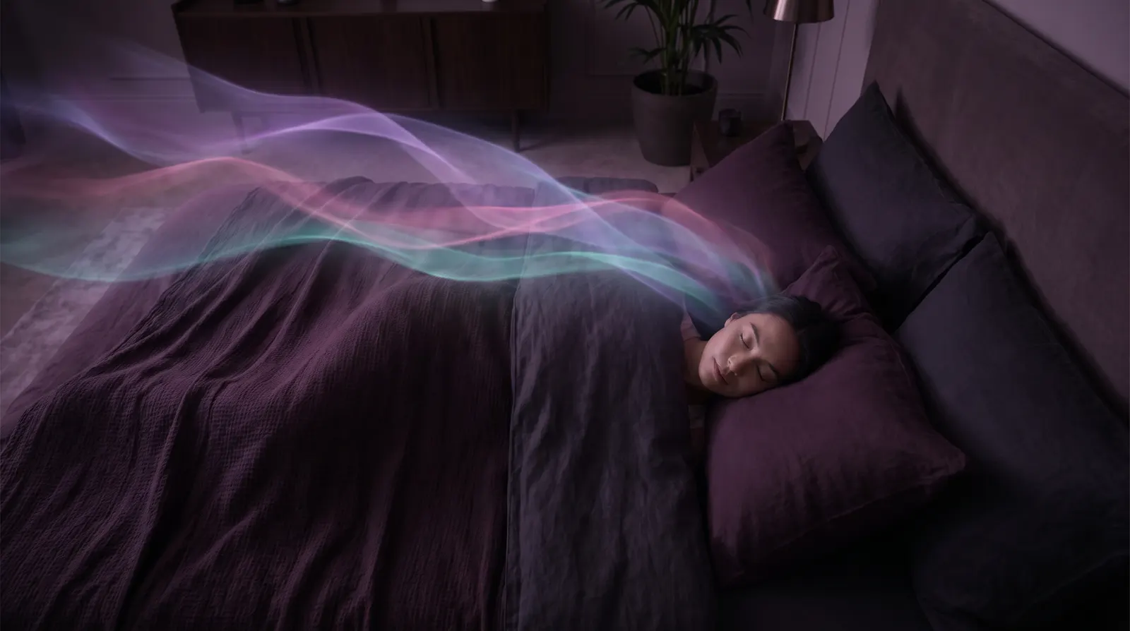 Sleeping figure in a dark aubergine bedroom with soft lavender and aqua ribbons of light drifting overhead.
