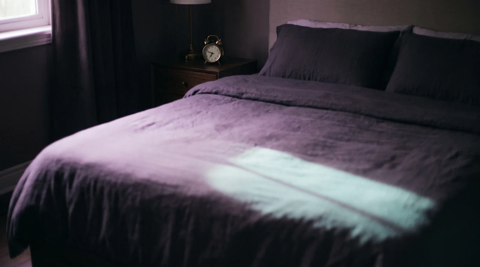 An afternoon bedroom in half-light, a bed bathed in soft lavender glow with a warm aqua band of window light across it.