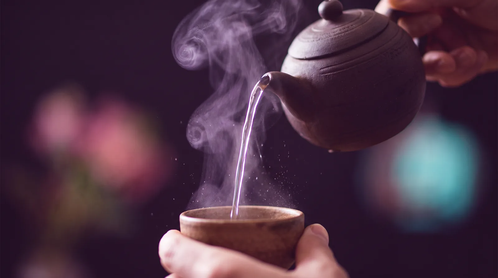 Hot water pouring in a thin luminous stream from a dark clay teapot into a small cup, steam curling in lavender light against a deep aubergine background.