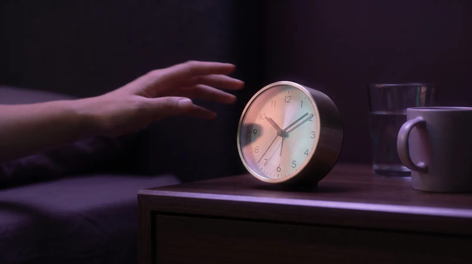 An alarm clock glowing softly on a nightstand in deep aubergine morning light.