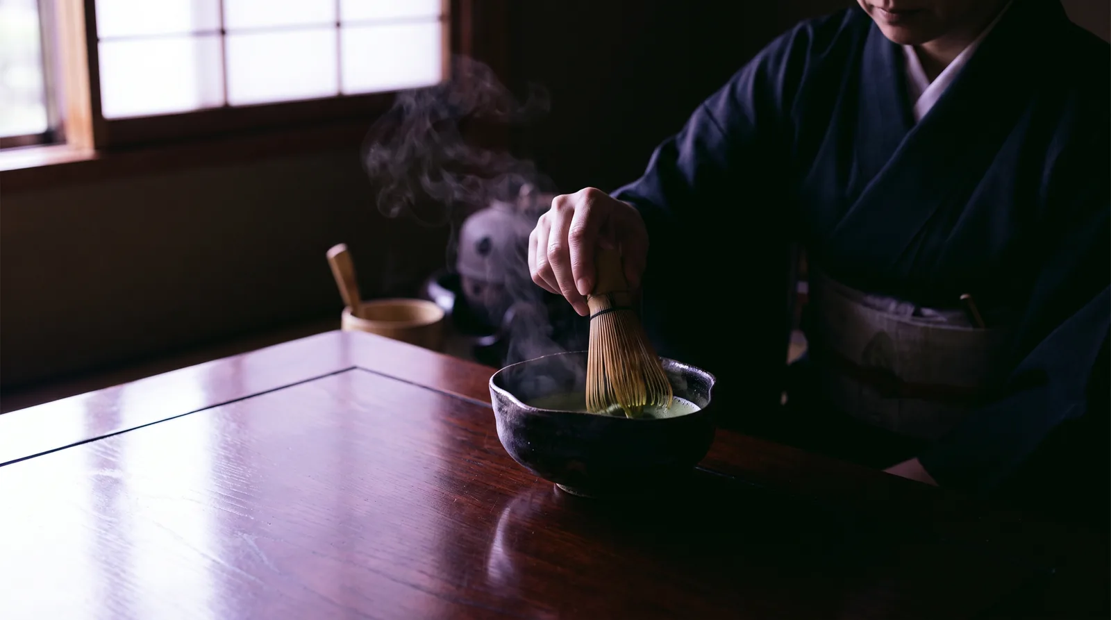 A matcha bowl and bamboo whisk in a beam of soft light, steam rising.