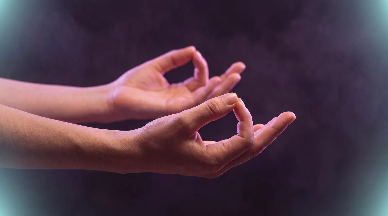 Two hands resting in a meditation mudra, thumb and forefinger touching, lit by soft lavender and rose light against a deep aubergine background.