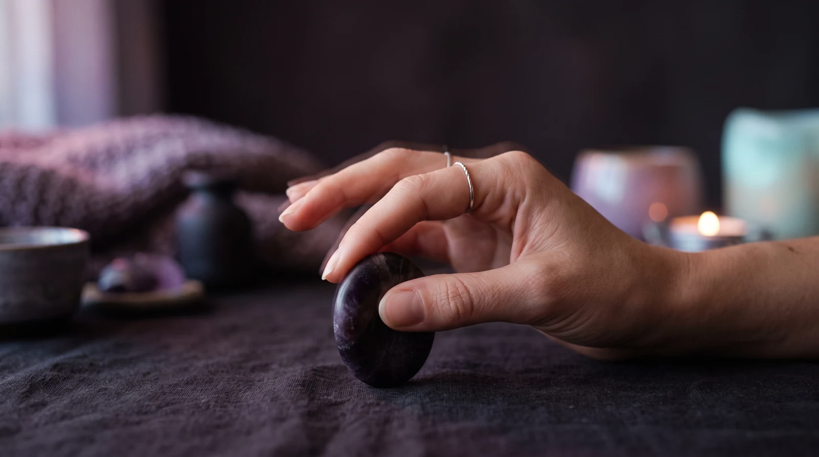 A close-up of a hand gently rolling a smooth fidget object, fingers in soft motion with faint lavender trails, against a dark aubergine background.