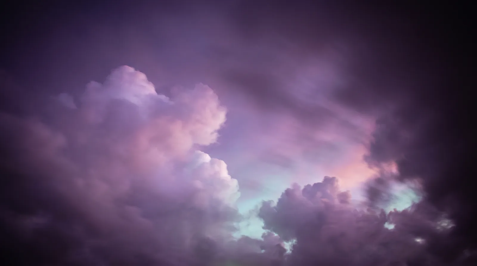 Vast soft clouds drifting across a deep aubergine twilight sky, their edges glowing lavender, rose and aqua.