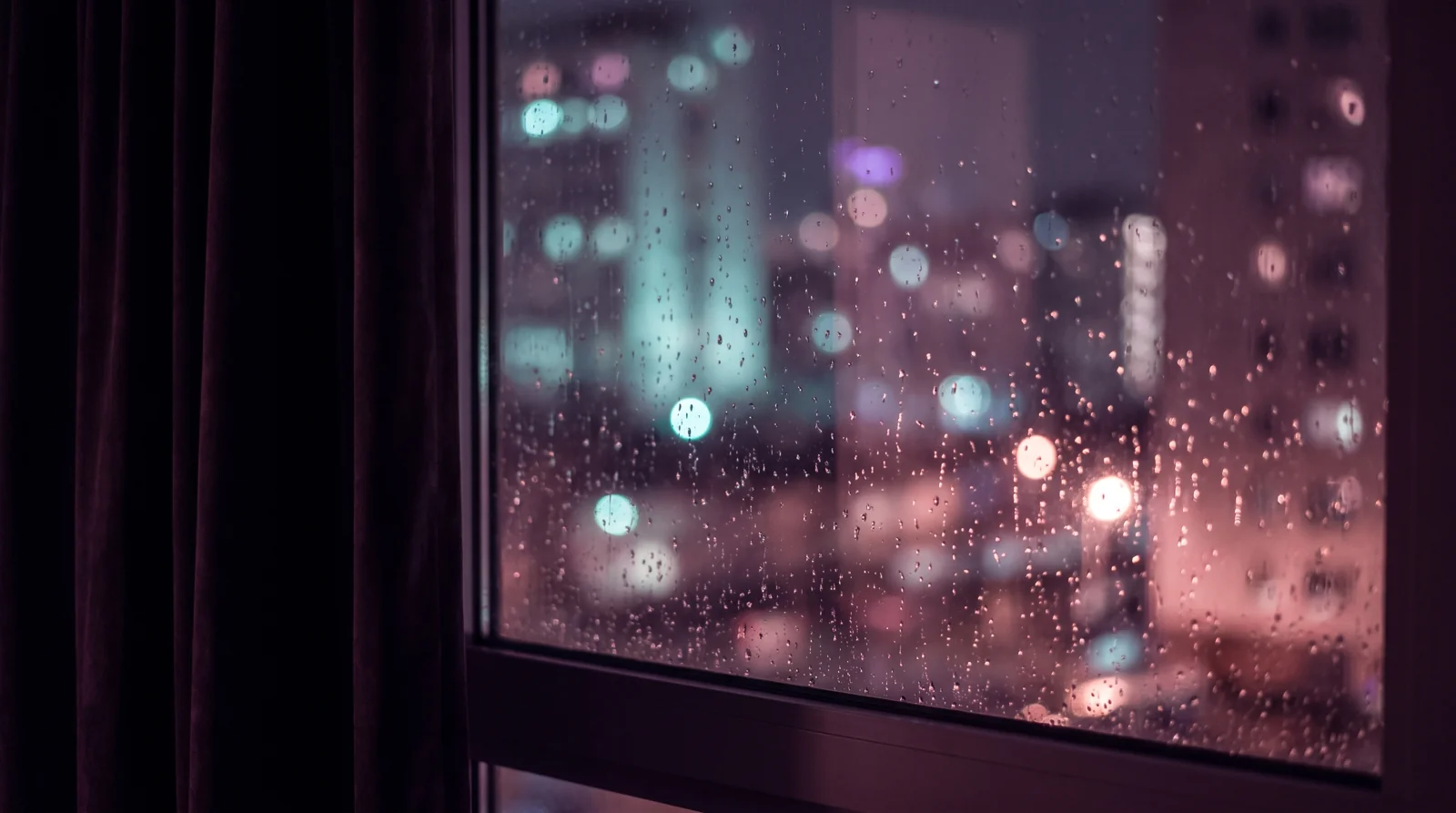 A rain-speckled window at night from inside a dark room, city lights blurred into aqua, lavender and rose bokeh beyond the glowing droplets.