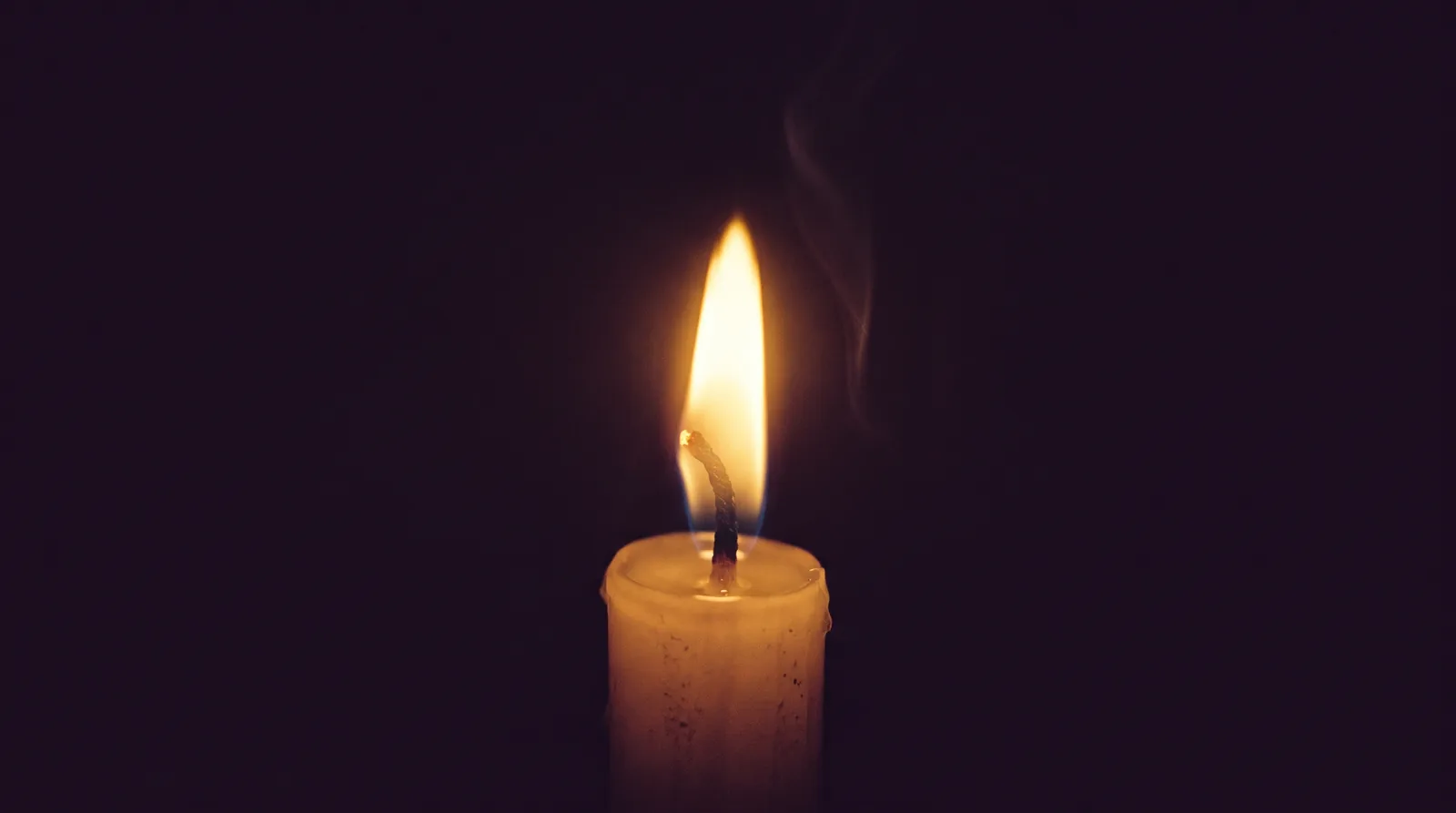 A single candle flame burning steadily in a dark room, the focus of trataka meditation.
