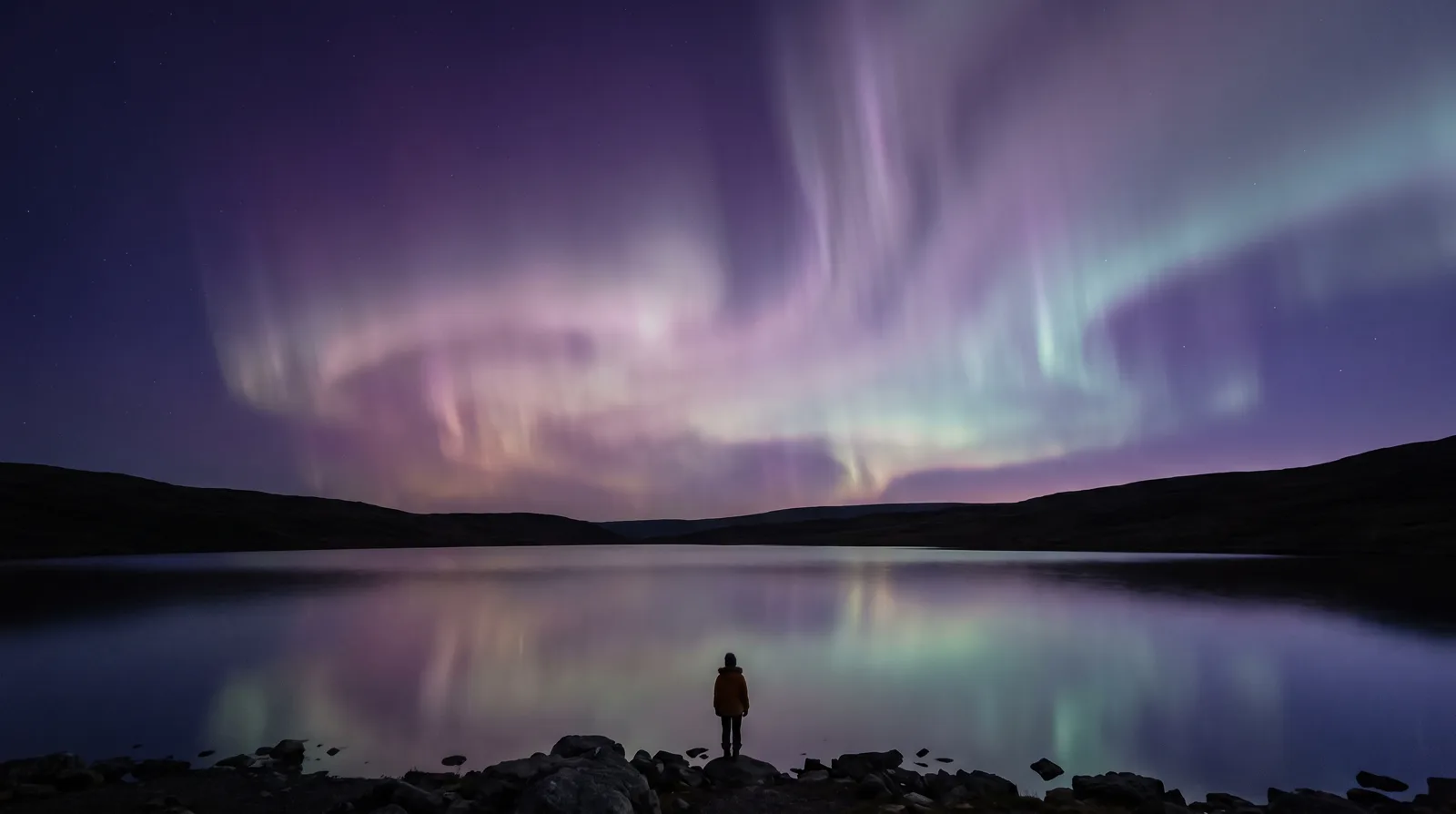 Aurora curtains in lavender, rose and aqua rippling over a dark still lake at night.