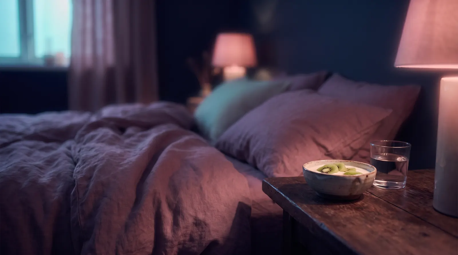 A small bowl of yogurt with kiwi and a glass of water on a nightstand in a dim aubergine bedroom.
