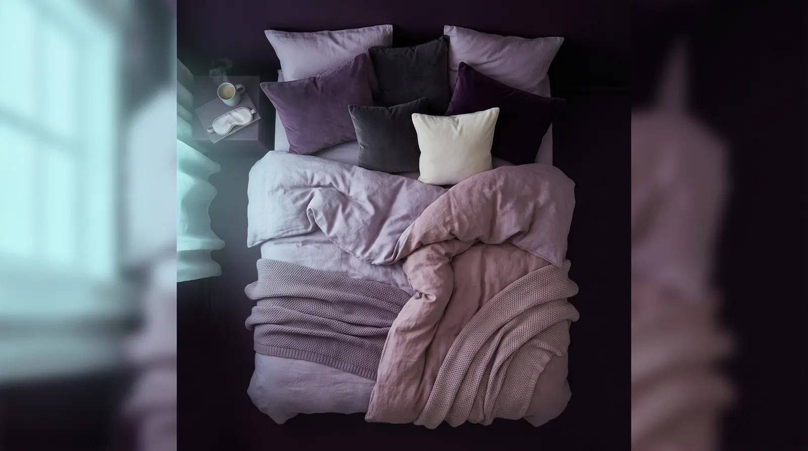 A person sleeping peacefully on their side under lavender bedding, seen from above in soft aubergine light.